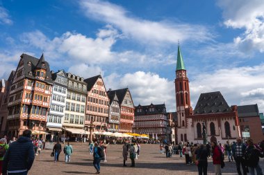 Frankfurt, Almanya 'daki Romerberg Meydanı' nda tarihi yarı ahşap binalar, Eski St. Nicholas Kilisesi, açık hava koltukları ve mavi gökyüzü altında canlı bir kalabalık yer alıyor..