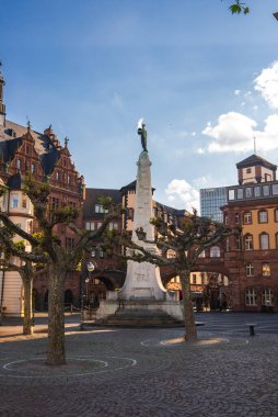 Frankfurt, Almanya 'da bir meydan, yüksek bir kaide üzerinde merkezi bir heykel, süslü cepheli tarihi binalar, budanmış ağaçlar ve modern yüksek binalar barındırır..