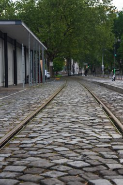 Almanya 'nın Frankfurt kentsel ortamında geçen, modern bir bina ve yemyeşil ağaçlarla çevrili, kaldırım taşlı bir cadde..