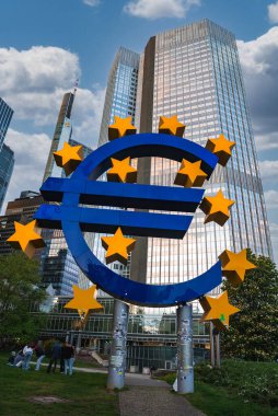 Frankfurt, Almanya 'daki Euro heykeli, Avrupa Merkez Bankası da dahil olmak üzere çağdaş gökdelenlerin önünde, yeşillik ve yakınındaki insanlarla birlikte duruyor..