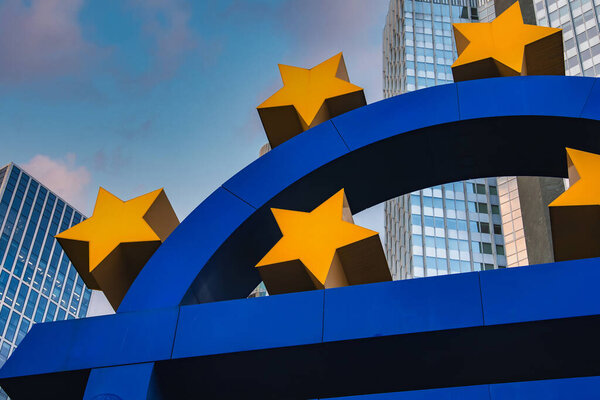 Перед современными стеклянными небоскребами во Франкфурте, Германия, стоит скульптура евро с желтыми звездами, демонстрирующая финансовый район города.