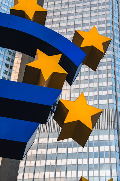 Крупный план символической скульптуры Евро во Франкфурте, Германия, с желтыми звездами и современным стеклянным небоскребом на заднем плане.