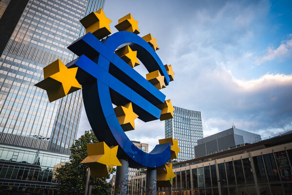 Скульптура евро во Франкфурте, Германия, окруженная желтыми звездами, с современными небоскребами и бывшей штаб-квартирой Европейского центрального банка.