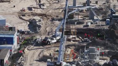 İşçiler makineleri çalıştırıyor ve Riga 'da bir inşaat sahasında dolaşıyorlar. Turnalar, beton mikserler ve köprü inşaatı..