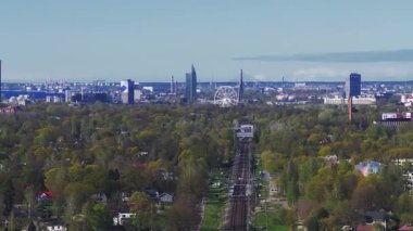 Riga, Letonya 'nın panoramik hava manzarası, Ulusal Kütüphane, Riga TV Kulesi, dönme dolap ve yeşil kentsel alanlardan geçen bir demiryolu.