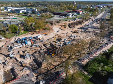 Vinçleri, sondaj ekipmanları ve malzemeleri olan aktif inşaat alanı. Çevresindeki kentsel ve yeşil alanlarda, yol ve araçlar yakınlarda.