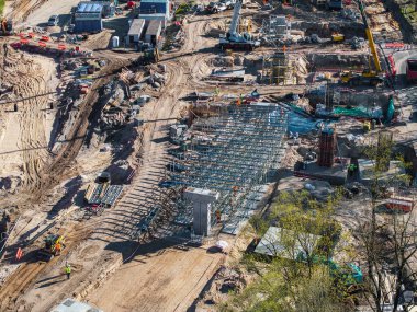 İskelesi, vinçleri, makineleri ve işçileri olan aktif bir inşaat alanı. Riga, Letonya 'da kısmen inşa edilmiş yapılar ve yeşillikler bölgeyi çevrelemektedir..