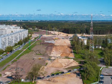 Riga 'da kum tepecikleri, ekipmanlar, bir konut binası, metal bir kule, ormanlık bir arka plan ve uzak kentsel yapılar ile inşaat alanı.