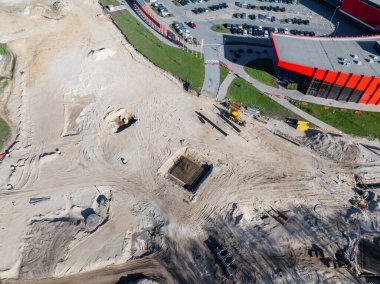 Riga, Letonya 'daki bir inşaat alanının havadan görünüşü, kumlu arazi, büyük bir kazı çukuru, makineler ve yakındaki modern kırmızı bina..