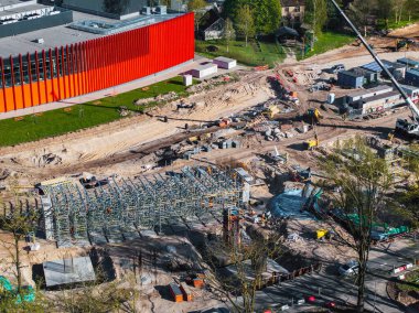 Riga, Letonya 'da etkin inşaat alanı, yapı iskelesi, ağır makineler, kırmızı modern bir bina ve proje alanına yakın çevredeki yeşillikler yer alıyor..