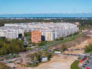 Riga, Letonya 'da konut blokları, yeşillik ve açık mavi gökyüzüne karşı makine ve malzemelerle yapılan inşaat faaliyetleri.