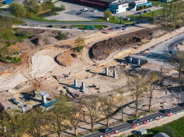Riga, Letonya 'daki bir inşaat alanının hava görüntüsü, beton sütunları, trafikli yolları, yeşil alanları ve arka planda kentsel altyapıyı gösteriyor..