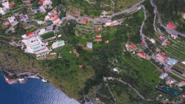 Yeşil tepeler boyunca dolambaçlı yollar, kırmızı çatılı binalar, tekneli küçük bir liman, teraslı manzaralar ve İtalya 'nın Amalfi kentindeki ekili bahçeler..