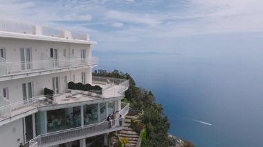 İtalya 'nın beyaz oteli, havuzu, yeşilliği, terasotta çatıları, uçurumları, sahil yolu ve denizdeki tekneleri ile Amalfi kıyı şeridini gösteren hava manzarası..