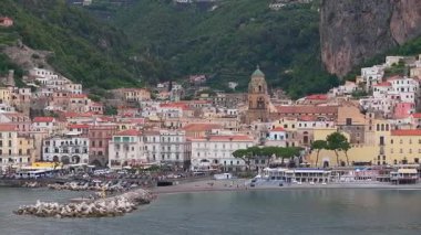 Renkli tepe binaları olan Amalfi kasabasının hava manzarası, çan kulesi, uçurumları, sakin denizi, İtalya 'da yemyeşil bir limanı olan bir kilise..