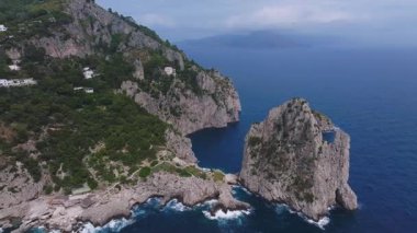 İtalya 'nın Capri kentinin havadan görünüşü, yeşil uçurumlar, beyaz bir bina, kayalık adalar ve sahil şeridi boyunca düzgün kamera hareketlerini gösteriyor..