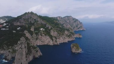 Capri 'nin kıyı şeridinin yavaş bir kısmı kayalıklarla, beyazlatılmış binalarla, yemyeşil ve bulutlar kısmen engebeli araziyi kaplıyor..