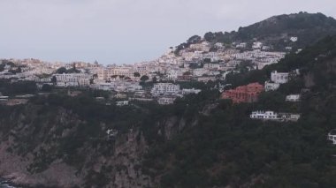 İtalya, Capri 'nin havadan görünüşü, engebeli uçurumları, beyazlatılmış binaları ve denizi olan bir yamaç kasabasını gösteriyor. Yumuşak hareket bulutlu sahneyi yakalar.