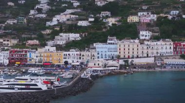 Capri, İtalya 'nın hava manzarası, feribot ve tekneli canlı bir marina, renkli tepe binaları, berrak mavi sular ve dramatik uçurumları gösteriyor..