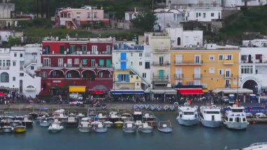 Marina Grande 'nin Capri, İtalya' daki hava görüntüsü, renkli binaları, rıhtım teknelerini ve rıhtımda yavaşça yürüyen kalabalığı gösteriyor..