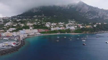 Capri, İtalya 'nın hava manzarası renkli binaları, gür tepeleri, sisli kayalıkları ve turkuaz Akdeniz sularındaki tekneleri olan bir kıyı kasabasını gösteriyor..