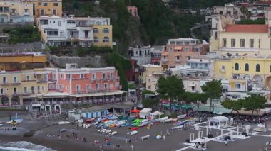 Positano, İtalya 'nın havadan görünüşü renkli teraslı binalar, tekneler ve şemsiyelerle dolu canlı bir sahil manzarası ve nazik kıyı faaliyetleri gösteriyor..