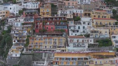 Positano 'nun Amalfi Sahili' ndeki hava manzarası, pastel binaların kayalıklardan, yeşillikten ve bulutlu gökyüzünden yavaşça inişini gösteriyor..