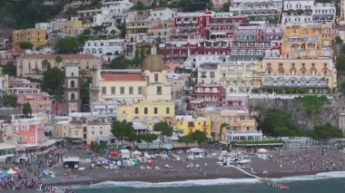 Positano, İtalya 'nın havadan görünüşü, renkli kayalık binalar, Santa Maria Assunta Kilisesi, tekne ve şemsiyeli canlı bir sahil..