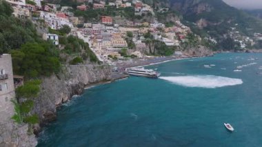 Positano 'nun İtalya' nın Amalfi Sahili 'ndeki hava manzarasında canlı binalar, verimli kayalıklar ve kıyıya yakın hareket eden bir tekne görülüyor..