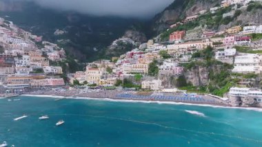 Positano, İtalya üzerindeki hava taraması kayalıklardaki renkli binaları, turkuaz suları, küçük tekneleri, yemyeşil tepeleri ve Amalfi Sahili boyunca sisli bulutları gösteriyor..