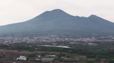 Pompeii 'nin antik harabeleri ve modern şehir manzarasının arka planında Vezüv Dağı var. Video, yemyeşil arazide yavaşça yayılıyor..
