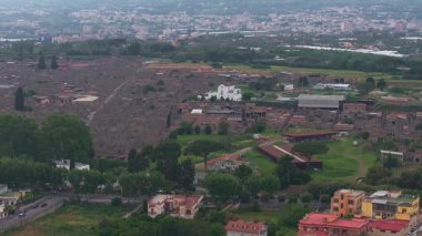 Pompei 'nin harabelerinin havadan görünüşü, caddelerin, duvarların ve binaların sergilenmesi. Sahnede yeşillik, modern sınırlar ve uzaktaki Vezüv Dağı yer alıyor..