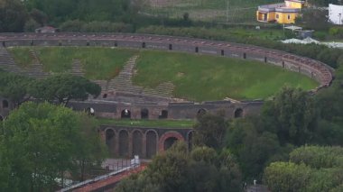 Pompeii, İtalya 'daki oval amfitiyatronun havadan görünüşü, yeşilliklerle çevrili. İnsanlar yakınlardaki patikalarda yürür, tarihi sahneyi hareketlendirirler..
