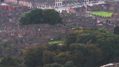 Pompei 'nin harabelerinin havadan görünüşü, caddelerin, duvarların ve binaların sergilenmesi. Yavaş tava, harabeler ve uzaktaki Vezüv Dağı arasındaki yeşilliği gözler önüne seriyor..