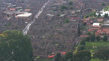 Pompeii 'nin taş harabelerinin ve modern binaların ve arka planda yeşillik olan kırmızı kiremitli çatılarının havadan görünüşü. Yavaş hareket sahneyi yakalar..