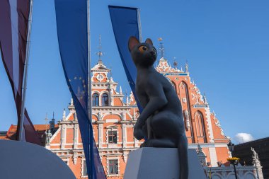 Riga, Letonya 'daki süslü Siyahların Evi' nde kırmızı tuğla cephesi ve beyaz ayrıntılarıyla Kedi heykeli ön planda yer alıyor..
