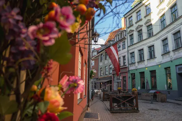 Riga 'nın eski kasabasındaki bir kaldırım taşı caddesinde renkli tarihi binalar, Letonya bayrağı, açık oturaklı küçük kafeler ve canlı çiçekler yer alıyor..