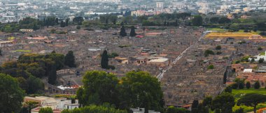 Pompei 'nin antik harabelerinin havadan görünüşü, arka planda taş yapılar, sokaklar, bir amfi tiyatro ve modern binalar yer alıyor..