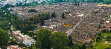 Pompeii 'nin İtalya' daki antik harabelerinin hava görüntüsü, yeşil ve modern binalarla çevrili amfitiyatro, sokak ve yapıları içeriyor..