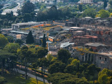 Pompei 'nin taştan yapılar ve sütunlarla dolu antik harabelerinin havadan görünüşü, arka planda yemyeşil ve modern kentsel altyapı arasında yer alıyor..