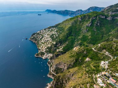İtalya, Amalfi 'nin hava manzarası, yeşil tepeli uçurumları, beyaz binaları, virajlı yolları ve Tyrhenian Denizi' ndeki tekneleri gösteriyor..