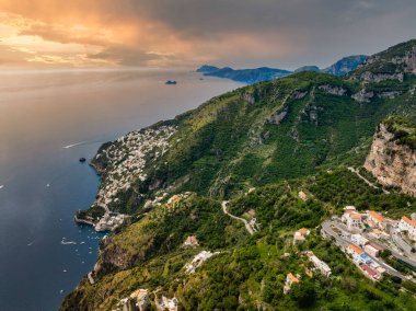 İtalya 'nın Amalfi Sahili' ndeki Amalfi kasabasının hava manzarasında kayalıklar, yeşil tepeler, beyazlatılmış binalar, lüks bir otel ve Tyrhenian Denizi 'ndeki tekneler yer alıyor..