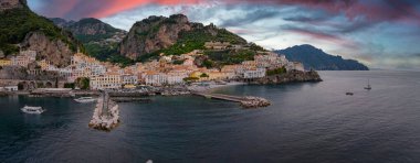 İtalya, Amalfi 'nin havadan görünüşü, tepe kenarındaki binalar, Tyrhenian Denizi' ne uzanan bir rıhtım, limandaki botlar, ve tepedeki lüks bir otel..