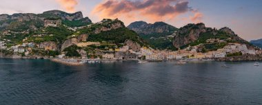 Uçurumlar, yeşil tepeler, renkli binalar, lüks bir otel, tekneli bir marina ve Tyrhenian Denizi üzerinde gün batımının yer aldığı İtalya, Amalfi 'nin hava manzarası..