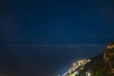 Geceleri Amalfi Sahili 'nde kıyı şeridini, engebeli uçurumları, yemyeşil otlakları ve yıldızlı gökyüzünün altındaki Tyrhenian Denizi' ni izleyen sıcak ışıklar görülür..