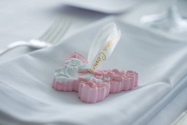 Çiçek detaylarıyla dekoratif haç şeklinde süslemeler ve katlanmış bir peçetenin üzerindeki melek motifi, rafine bir yemek düzeninde çatal ve cam ile..