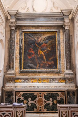 Amalfi kilisesindeki süslü bir sunakta mermer sütunlar, karmaşık taş işçiliği ve renkli kaplamalar ile çerçevelenmiş canlı bir dini tablo yer alıyor..