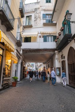 İtalya 'nın Amalfi kentindeki işlek bir kaldırım taşı caddesi. Tarihi binalar, renkli vitrinler ve caddenin yukarısında kapalı bir geçit var..