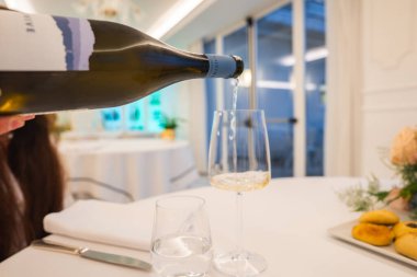 Beyaz çarşaflar, pastalar ve parlak bir Amalfi restoranının içindeki çiçeklerle dolu bir masanın üzerine bir şişe beyaz şarap dökülüyor..