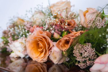 Şeftali ve pembe güller içeren çiçek aranjmanı, beyaz bebek nefesi, ve tarafsız bir arkaplanda yeşil yapraklar..